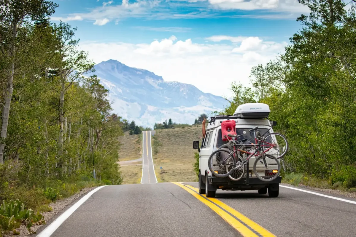 Van aménagé sur une route de montagne, équipé de vélos et d’équipement de camping, symbolisant un road trip hors des sentiers battus et l’aventure nomade.