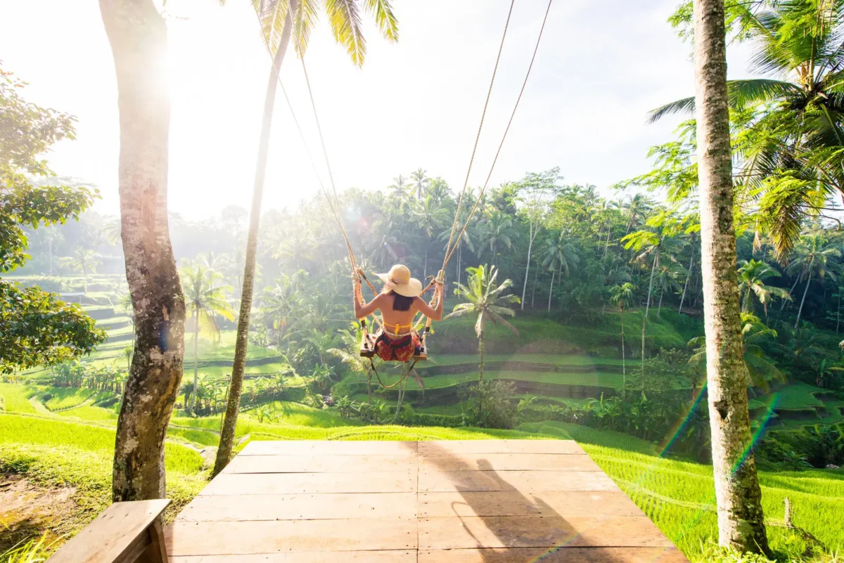 Voyageuse sur une balançoire au-dessus des rizières de Tegalalang à Bali, profitant d’une vue panoramique sur la jungle tropicale.