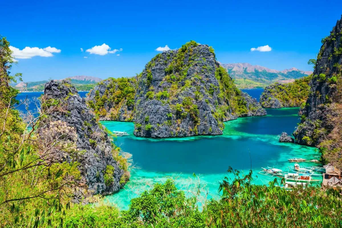Vue aérienne de Coron, aux Philippines, avec ses eaux turquoise, ses formations rocheuses spectaculaires et ses bateaux traditionnels naviguant dans le lagon.